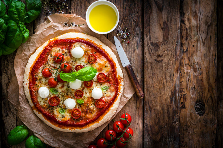 Ball of Italian pizza dough on floured wooden surface, ready for baking with rustic ingredients in background