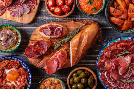 Spanish Jamón Serrano and Ibérico thinly sliced on wooden board with olives and bread – premium cured meats from Spain