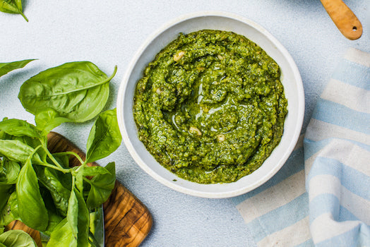 Assorted jars of authentic Italian pesto with basil, truffle, and sun-dried tomato, displayed on a rustic wooden board with fresh ingredients.